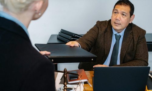 A professional business interaction at a desk with document exchange.
