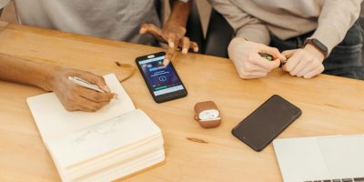 Teamwork at a table using smartphones, notebooks, and laptops to collaborate in an office setting.