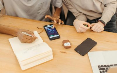 Teamwork at a table using smartphones, notebooks, and laptops to collaborate in an office setting.